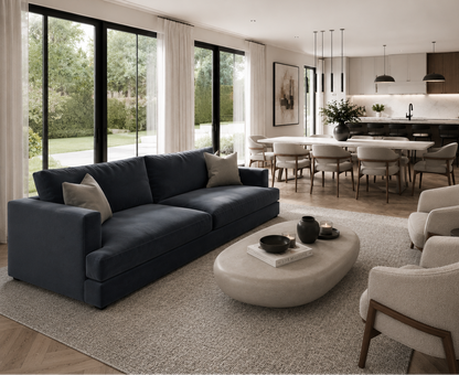 Modern living room with a dark blue sofa, white chairs, and a kitchen in the background.