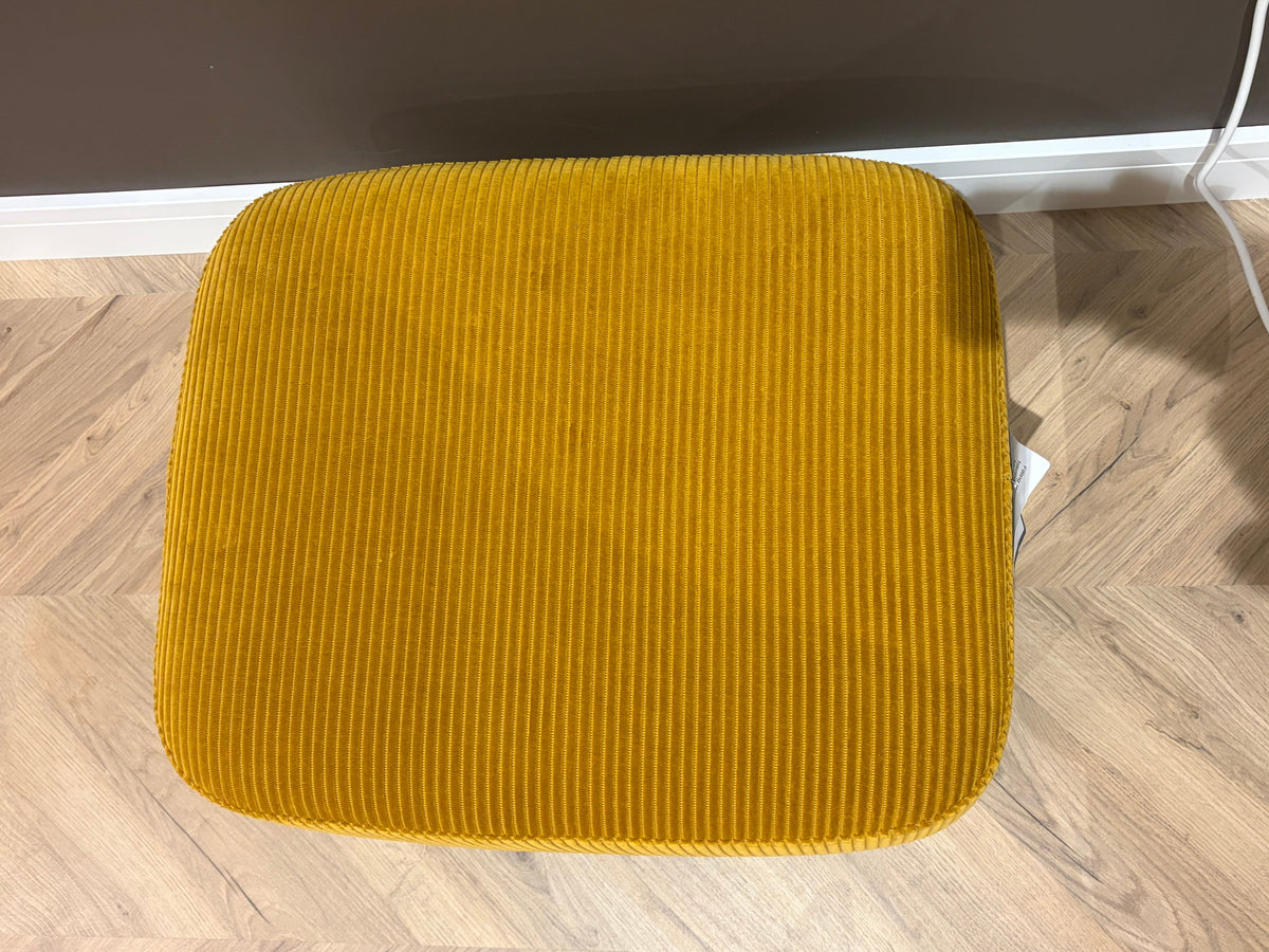 A mustard yellow corduroy upholstered stool or ottoman shown from a top-down perspective on a light wood herringbone floor.